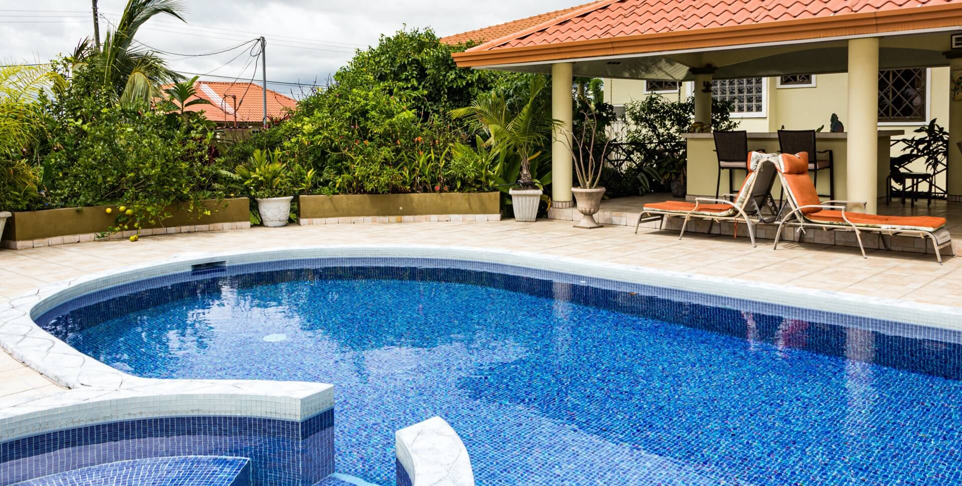 A swimming pool with a curved shape and blue mosaic tiles, surrounded by lounge chairs and a covered bar area.