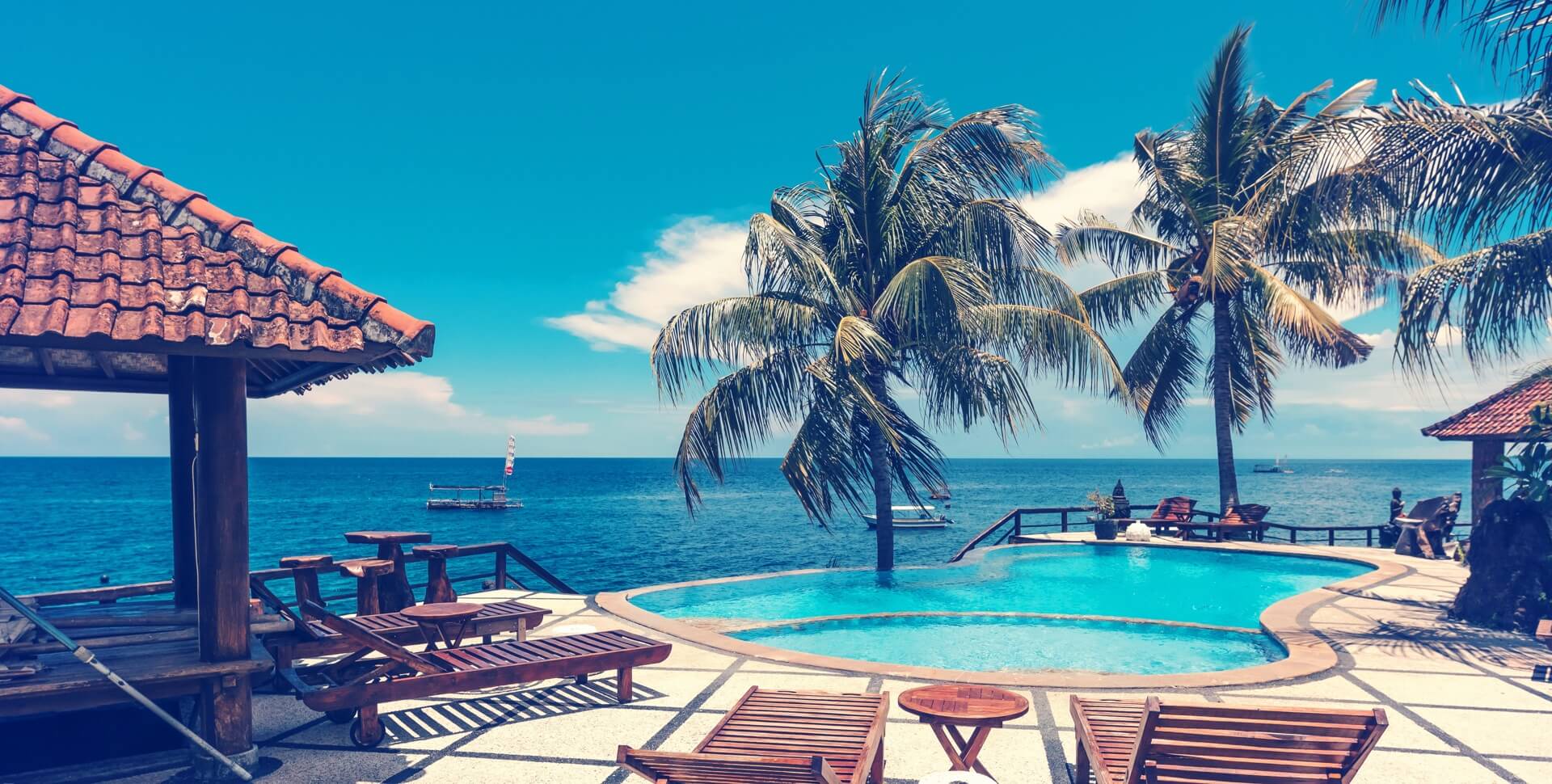 A tropical pool area with lounge chairs, palm trees, and an ocean view.