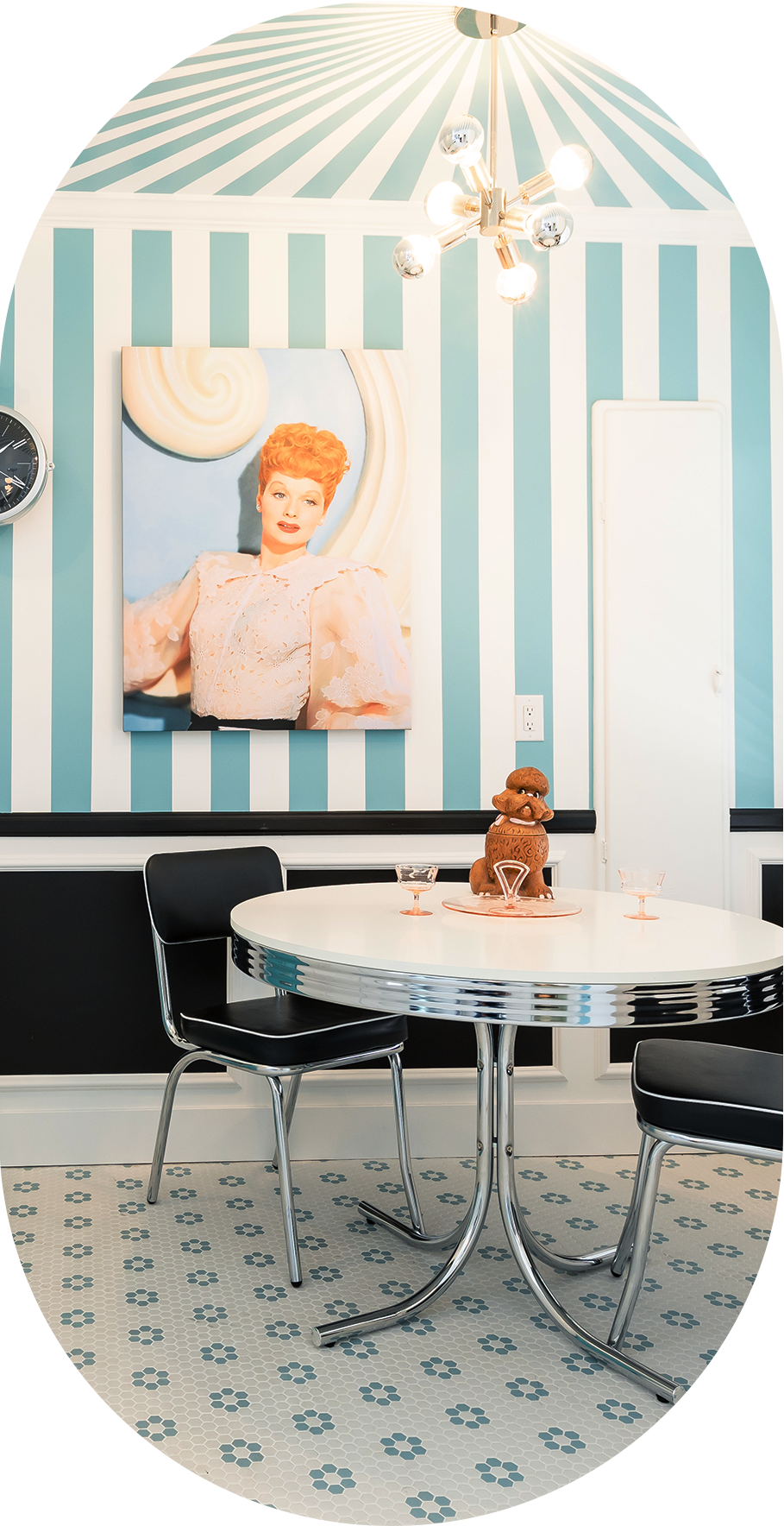 A dining area with a round table and chairs, striped walls, and a chandelier.