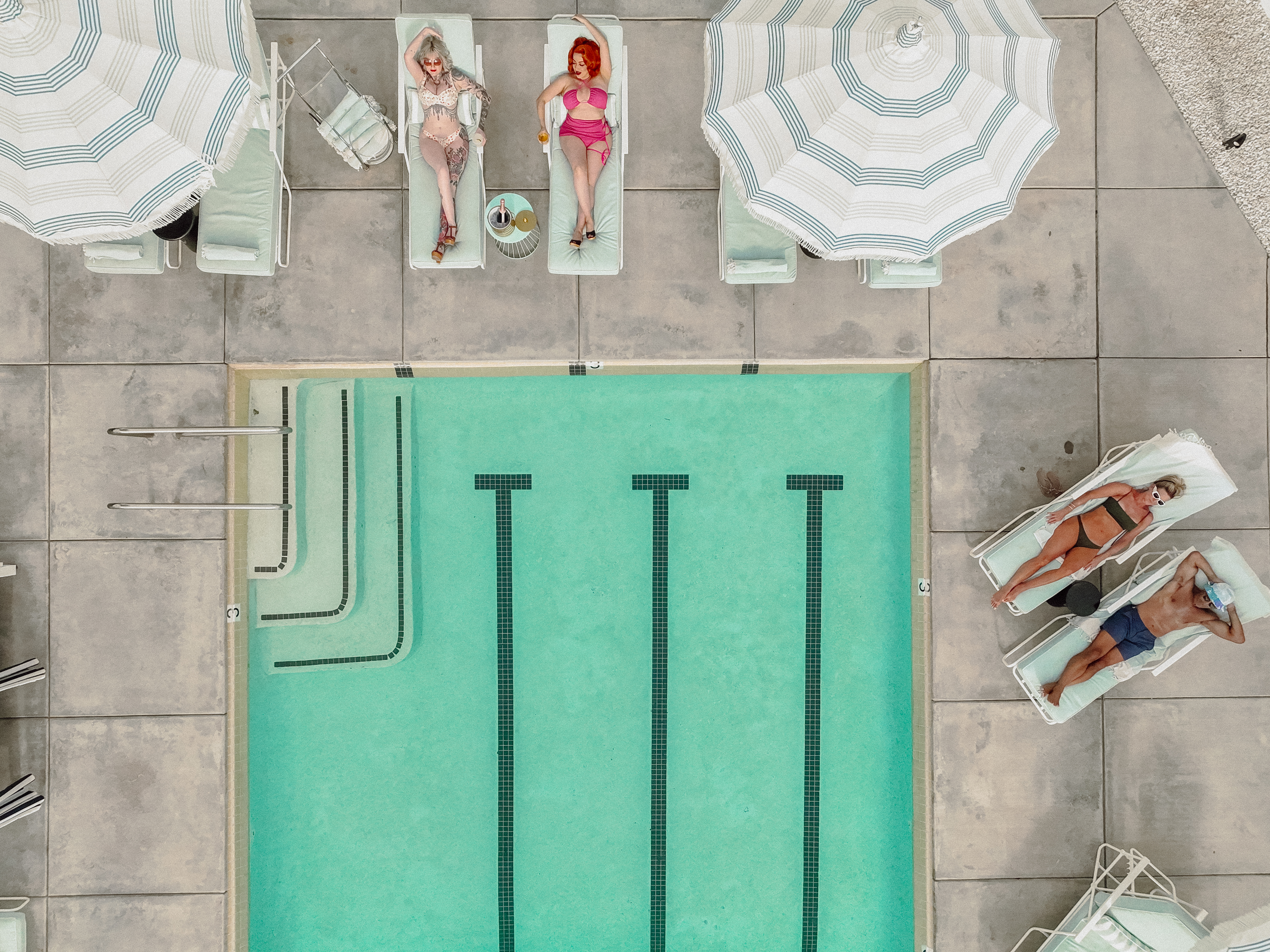 An overhead view of a pool with people lounging on chairs under umbrellas.